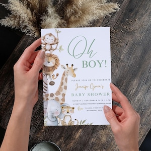 Puede incluir: Una invitaci&oacute;n a un baby shower con el texto "Oh Boy!" en verde. La invitaci&oacute;n presenta ilustraciones de animales de la jungla, incluyendo un mono, un le&oacute;n, una cebra, una jirafa, un elefante y un leopardo. La invitaci&oacute;n es sostenida por una persona.