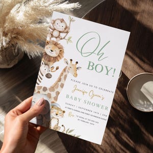 Puede incluir: Una invitaci&oacute;n a un baby shower con el texto "Oh BOY!" en verde. La invitaci&oacute;n presenta ilustraciones de animales de safari, incluyendo un mono, un le&oacute;n, una cebra, una jirafa, un elefante y un leopardo. La invitaci&oacute;n es sostenida por una persona.