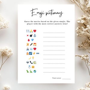 May include: A white Emoji Pictionary game sheet with the title in cursive script. The game includes a series of emojis to guess movies from, with lines for answers and a space for the total score. Decorative dried flowers are in the background.