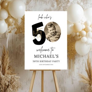 May include: A white welcome sign with black text and a gold accent. The sign says "Look who's 50 fifty" with a photo of a young boy. The sign also says "Welcome to Michael's 50th Birthday Party 22nd September 202X".
