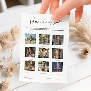 May include: A white card with the text "How old was she?" in black script. The card features nine photos of women at different ages, with spaces for names and total correct answers. The card is held by a hand.