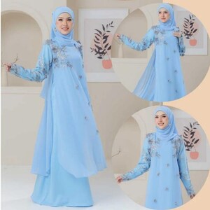 May include: A light blue dress with long sleeves and a matching head covering. The dress features silver floral embroidery on the sleeves and bodice. The dress has a flowing, layered design.