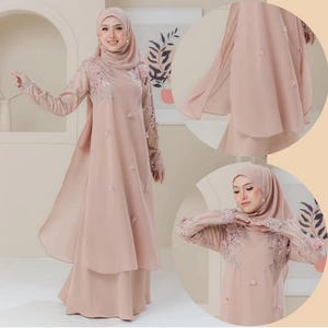 May include: A blush-colored formal dress with long sleeves and a matching head covering. The dress features floral embroidery on the sleeves and bodice, with delicate floral embellishments. The dress has a flowing skirt and a sheer overlay.