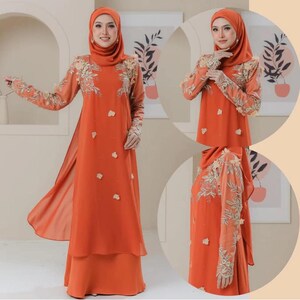 May include: An orange dress with long sleeves and a matching head covering. The dress features floral embroidery on the sleeves and bodice, with small floral accents scattered across the front. The dress has a layered skirt and a flowing, open front design.