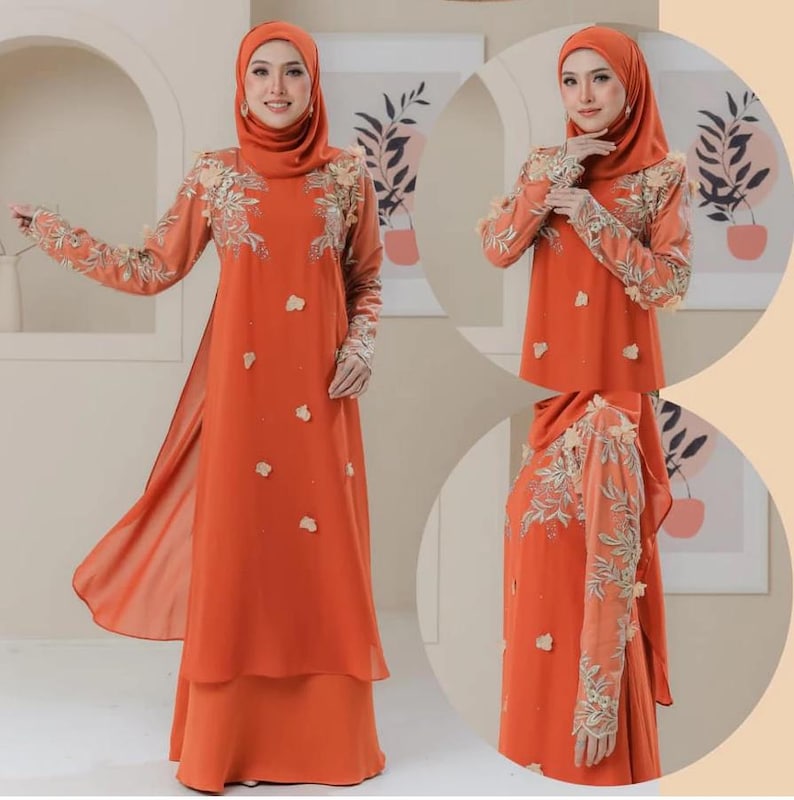 May include: An orange dress with long sleeves and a matching head covering. The dress features floral embroidery on the sleeves and bodice, with small floral accents scattered across the front. The dress has a layered skirt and a flowing, open front design.