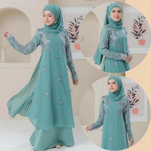 May include: A teal-colored formal dress with long sleeves and floral embroidery. The dress features a flowing, layered design with a matching head covering. The sleeves have intricate silver embroidery, and the dress is adorned with small, decorative accents.