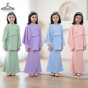 Può includere: Quattro ragazze con abiti coordinati dai colori pastello. Ogni outfit include un top a maniche lunghe con una sovrapposizione a forma di mantello e una gonna lunga. I top hanno un abbellimento decorativo. Gli abiti sono nelle tonalità di verde, viola, blu e rosa. Il marchio "Ayra & Aydan" è visibile.