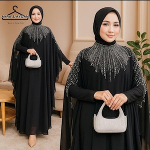May include: A black maxi dress with long sleeves and a high neckline, embellished with silver-colored beadwork. The dress features a flowing cape-like design and is paired with a small, light-colored handbag. The image includes the text "AYRA & AYDAN".