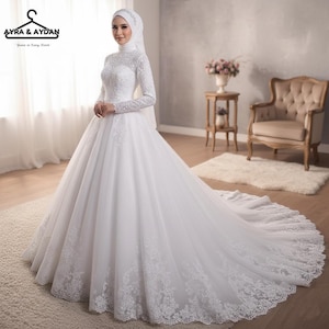 Puede incluir: Un vestido de novia blanco con mangas largas y falda amplia. El vestido presenta intrincados detalles de encaje en el corpiño, las mangas y el dobladillo. La novia lleva un hiyab y un velo blancos. El vestido tiene una larga cola. El logo "AYRA & AYDAN" está en la esquina superior izquierda.