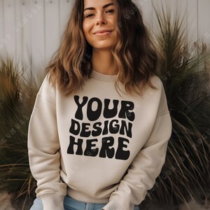 Puede incluir: Una sudadera beige con el texto "YOUR DESIGN HERE" en letras negras de estilo retro.