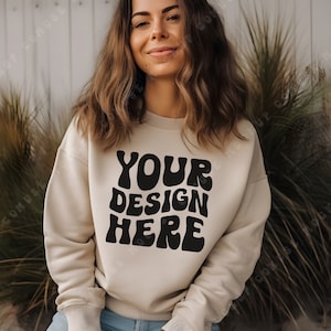 Puede incluir: Una sudadera beige con el texto "YOUR DESIGN HERE" en letras negras de estilo retro.