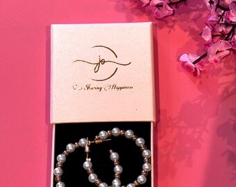 May include: A white gift box with a gold logo that says "Sharing Happiness" and a pair of gold hoop earrings with white pearls.