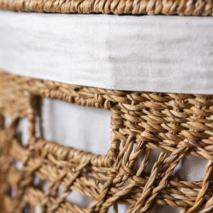 May include: Close-up of a woven basket with a natural, light brown color. The basket has a textured surface and a white fabric lining the interior. The weave pattern is intricate, with a sturdy, open design.