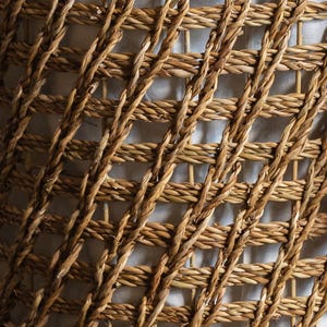 May include: Close-up of a woven basket texture. The basket is made of natural-colored, tightly woven fibers, creating a grid-like pattern. The fibers are a warm, earthy tone, with variations in color and texture.