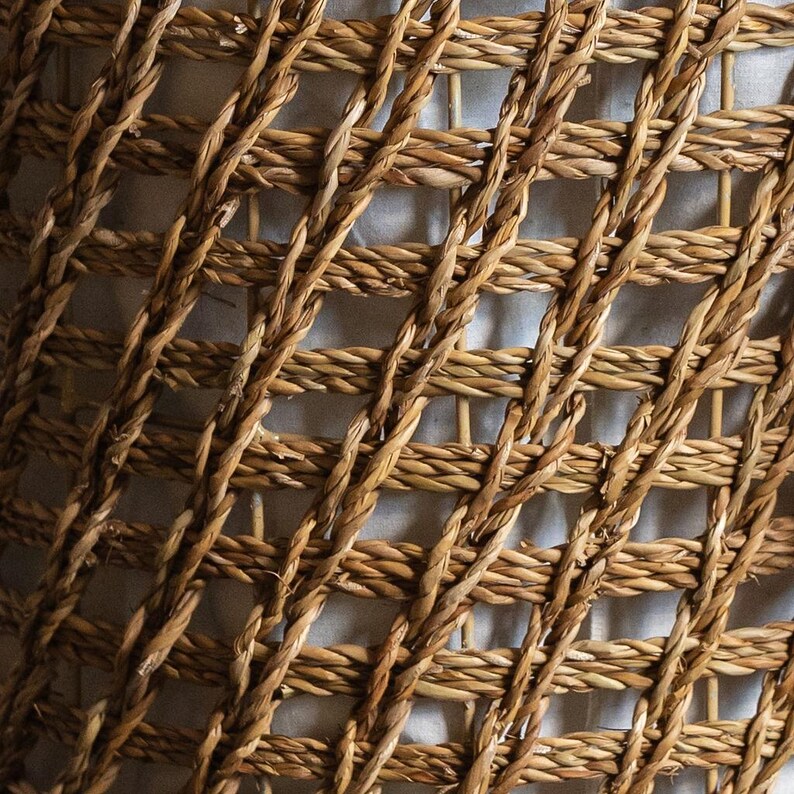 May include: Close-up of a woven basket texture. The basket is made of natural-colored, tightly woven fibers, creating a grid-like pattern. The fibers are a warm, earthy tone, with variations in color and texture.