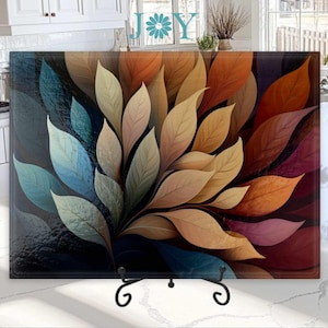 May include: A glass cutting board with a colorful abstract design of overlapping leaves in shades of blue, green, brown, orange, and red.
