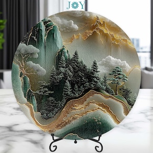 May include: A round decorative plate with a gold and green mountain landscape design. The plate features a stylized depiction of mountains, trees, and clouds. The plate is on a black stand.