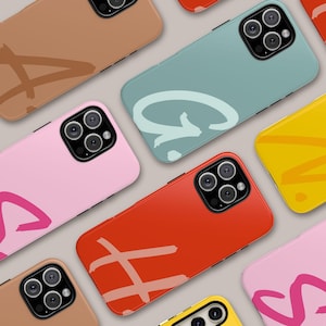 May include: Assortment of colourful phone cases with abstract designs. Each case features a different colour and a unique graphic, including a pink case with a heart, a red case with a hashtag, and a blue case with a letter G.