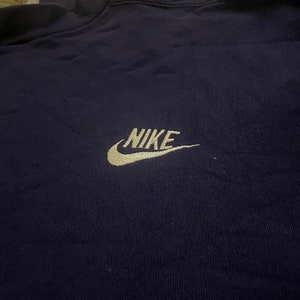 Op de afbeelding: Een marineblauw sweatshirt met een gouden geborduurd Nike-logo.