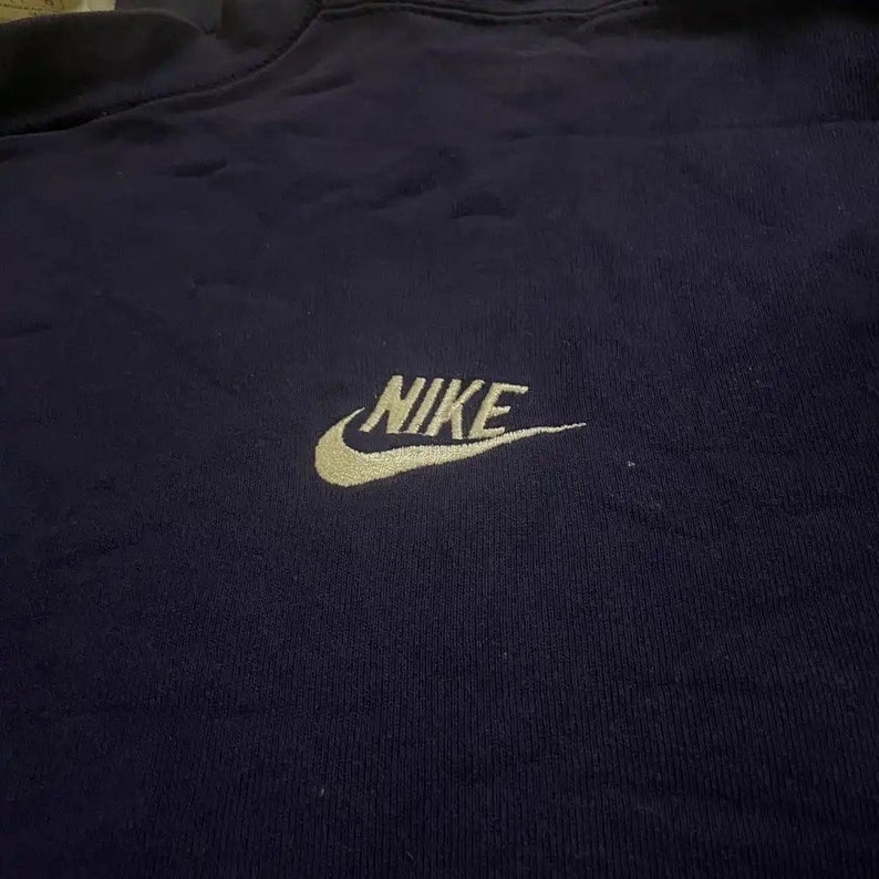 Op de afbeelding: Een marineblauw sweatshirt met een gouden geborduurd Nike-logo.