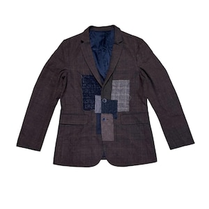 May include: A brown blazer with a plaid pattern and a patchwork design on the front. The blazer has a navy blue interior and two front pockets. The patchwork includes squares of navy, grey, and brown fabrics.