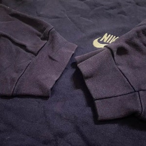 Op de afbeelding: Een marineblauw longsleeve shirt met een gouden Nike-logo op de borst. Het shirt heeft geribbelde manchetten en een klassieke pasvorm.