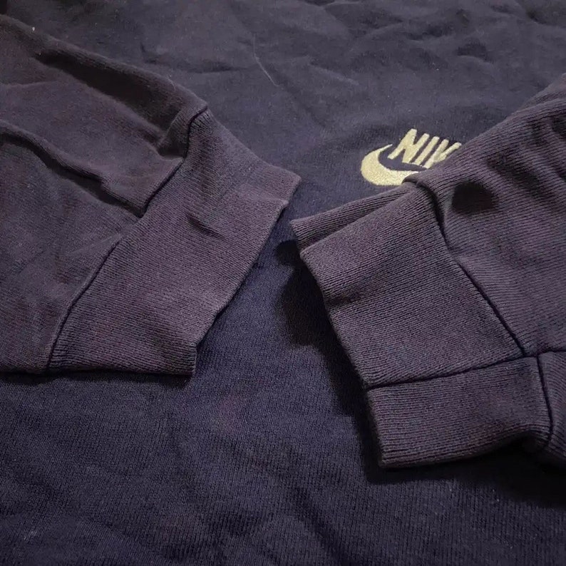 Op de afbeelding: Een marineblauw longsleeve shirt met een gouden Nike-logo op de borst. Het shirt heeft geribbelde manchetten en een klassieke pasvorm.