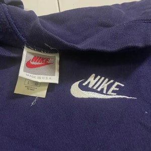 Op de afbeelding: Een donkerpaarse hoodie met een wit geborduurd Nike-logo op de voorkant. De hoodie heeft een wit label met het Nike-logo en de tekst "Made in U.S.A." en "L G" erop.