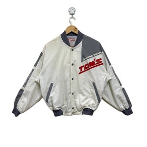 May include: A white and grey bomber jacket with the text "TOM'S RACING TEAM" and "ENGINEERING" on the sleeves.