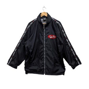 Puede incluir: Chaqueta negra con cremallera con un logotipo rojo que dice "Dog Town" y texto blanco a lo largo de las mangas que dice "Dog Town" repetidamente.