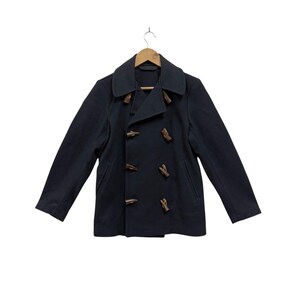 May include: A navy blue toggle coat with a double-breasted design. The coat features wooden toggles and a notched collar. The coat is hanging on a wooden hanger.