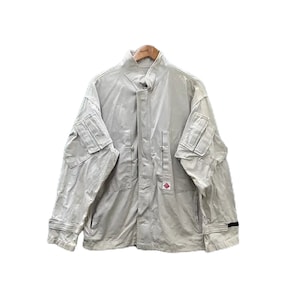 Puede incluir: Una chaqueta de trabajo beige claro con cierre de cremallera y dos bolsillos grandes en las mangas. La chaqueta tiene un logotipo en forma de diamante en la parte delantera.