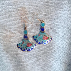 May include: A pair of silver-toned earrings with a fan-shaped design. The earrings feature a turquoise base with red floral accents and blue and gold trim. The earrings have a hook closure.