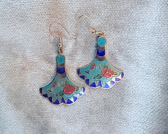 Può includere: Un paio di orecchini color argento con un design a forma di ventaglio. Gli orecchini presentano una base turchese con accenti floreali rossi e finiture blu e oro. Hanno una chiusura a gancio.