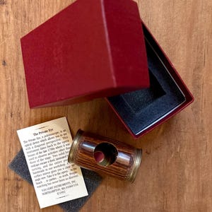 May include: A vintage polemoscope with a wooden barrel and brass accents, accompanied by a red box and a descriptive card. The text on the card reads "The Private Eye" and describes the device's function and history.