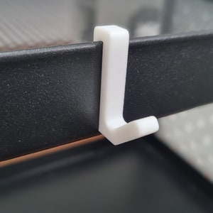 Peut inclure: Crochet blanc en plastique fixé à une étagère en métal noir.