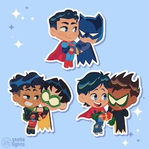 May include: Three sets of cartoon stickers featuring pairs of characters. One shows a hero in a blue suit and red cape holding a dark-clad hero. Another shows a character with dark hair holding a masked hero. The third shows a character holding a gift.