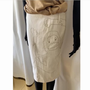 May include: A white skirt with a black line drawing of a monkey on it.