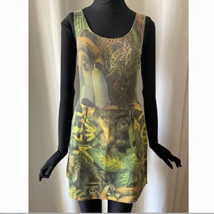 May include: A sleeveless green and yellow denim dress with a jungle print featuring a toucan, a monkey, and a leopard. The dress has a zipper on the side and the word "VIBERA" is printed on the bottom.