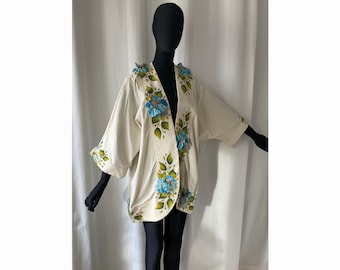 Könnte beinhalten: Ein weißer Leinen-Kimono mit blauer und grüner Blumenstickerei. Der Kimono hat einen V-Ausschnitt und Dreiviertelärmel.