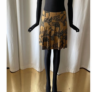 May include: A brown and black patterned skirt with a pleated design. The skirt is knee-length and has a fitted waist.