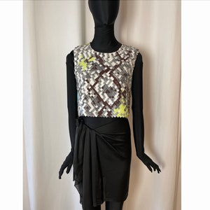 Peut inclure: Un haut sans manches avec un motif géométrique dans les tons de gris, blanc, marron et jaune. Le haut est court et a un col rond.