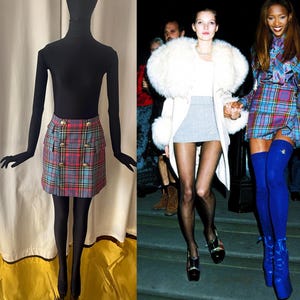 May include: A tartan mini skirt in red, blue, and green, with gold buttons, displayed on a mannequin. The image also shows a vintage photo of two women wearing similar tartan skirts, one with a white fur coat and the other with blue thigh-high boots.