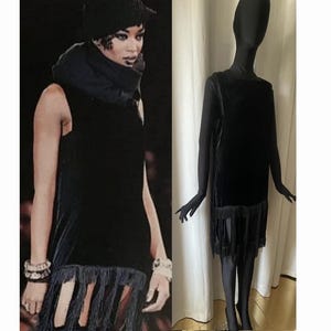 Puede incluir: Un vestido de flapper de terciopelo negro con ribete de flecos. El vestido es sin mangas y tiene un escote recto. Se muestra en un maniquí.