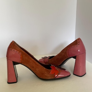 Peut inclure: Une paire de chaussures à talons en daim marron et rose avec un motif de feuille sur l'orteil. Les talons sont épais et les chaussures ont une pointe pointue.