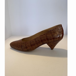Peut inclure: Escarpin en cuir marron avec un motif texturé en forme de crocodile. La chaussure a un bout pointu et un talon angulaire. Le talon mesure environ 5 cm.