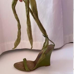 Op de afbeelding: Een groene sleehak sandaal met een bandje over de tenen en lange stoffen banden die om de enkel wikkelen. De sleehak is ongeveer 7.6 cm hoog. De sandaal heeft een gedempte groene kleur.