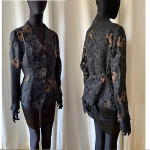 May include: A dark grey blazer with a floral pattern in shades of brown and grey. The blazer features a notched collar, button closure, and long sleeves. The garment is displayed on a mannequin.