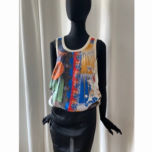 Peut inclure: Un débardeur blanc sans manches avec un imprimé abstrait coloré. L'imprimé présente des formes géométriques, des motifs floraux et une variété de couleurs, notamment le bleu, le vert, le rouge, l'orange et le jaune.