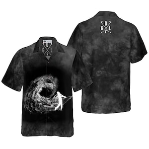 May include: Black and white golf-themed button-up shirt. The front features a golfer silhouette and swirling smoke design. The back has a golf club graphic. The shirt has the word "GOLF" on the collar.